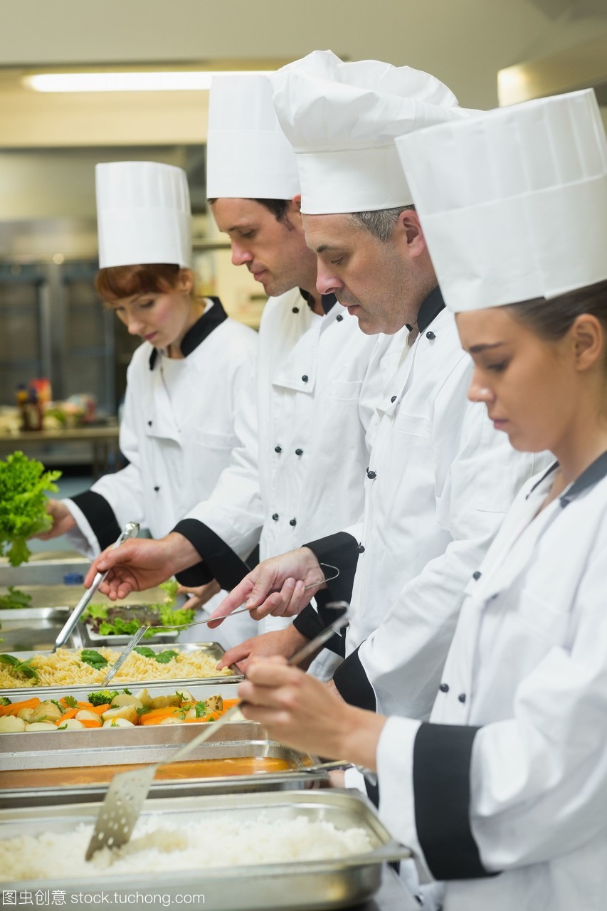 四個(gè)廚師在忙碌的廚房里服務(wù)托盤(pán)